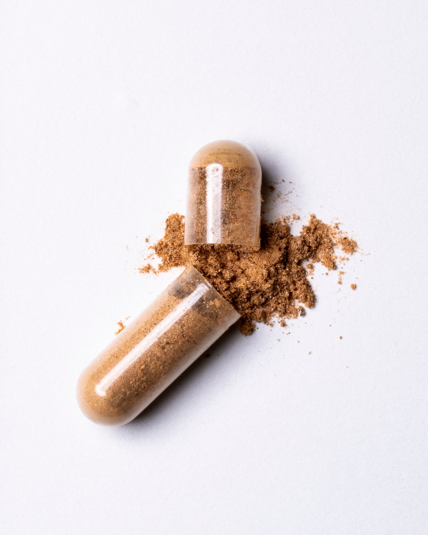 Two transparent capsules filled with brown powder on a white background